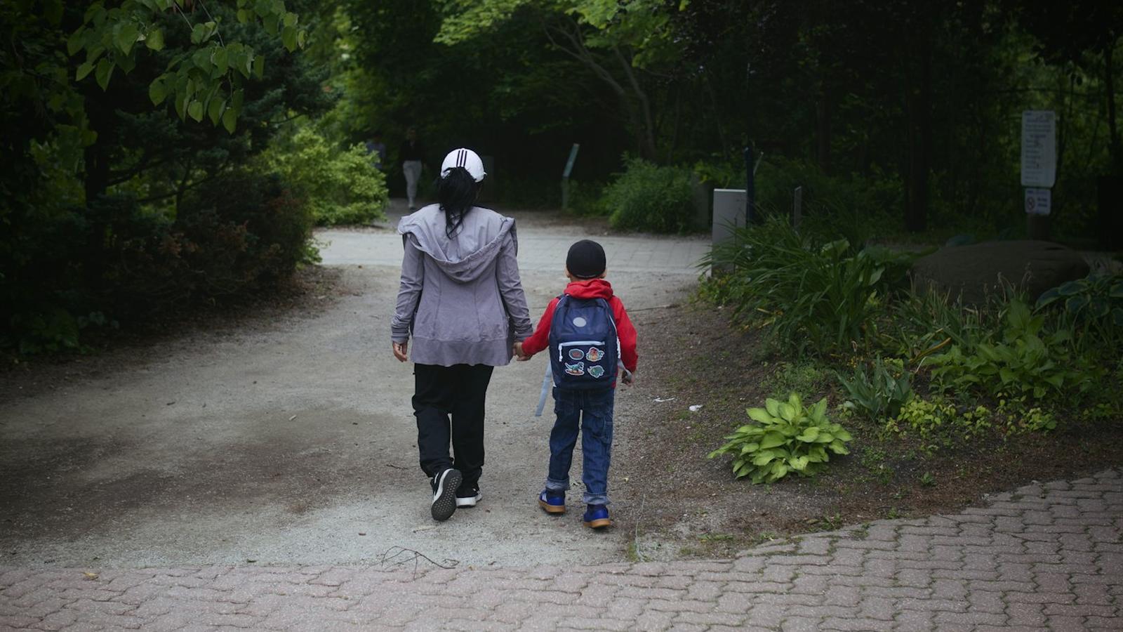 Une femme et un jeune enfant, vus de dos, marchent main dans la main sur une allée de parc : le même chauffeur, semaine après semaine, pour ceux que vous confiez.