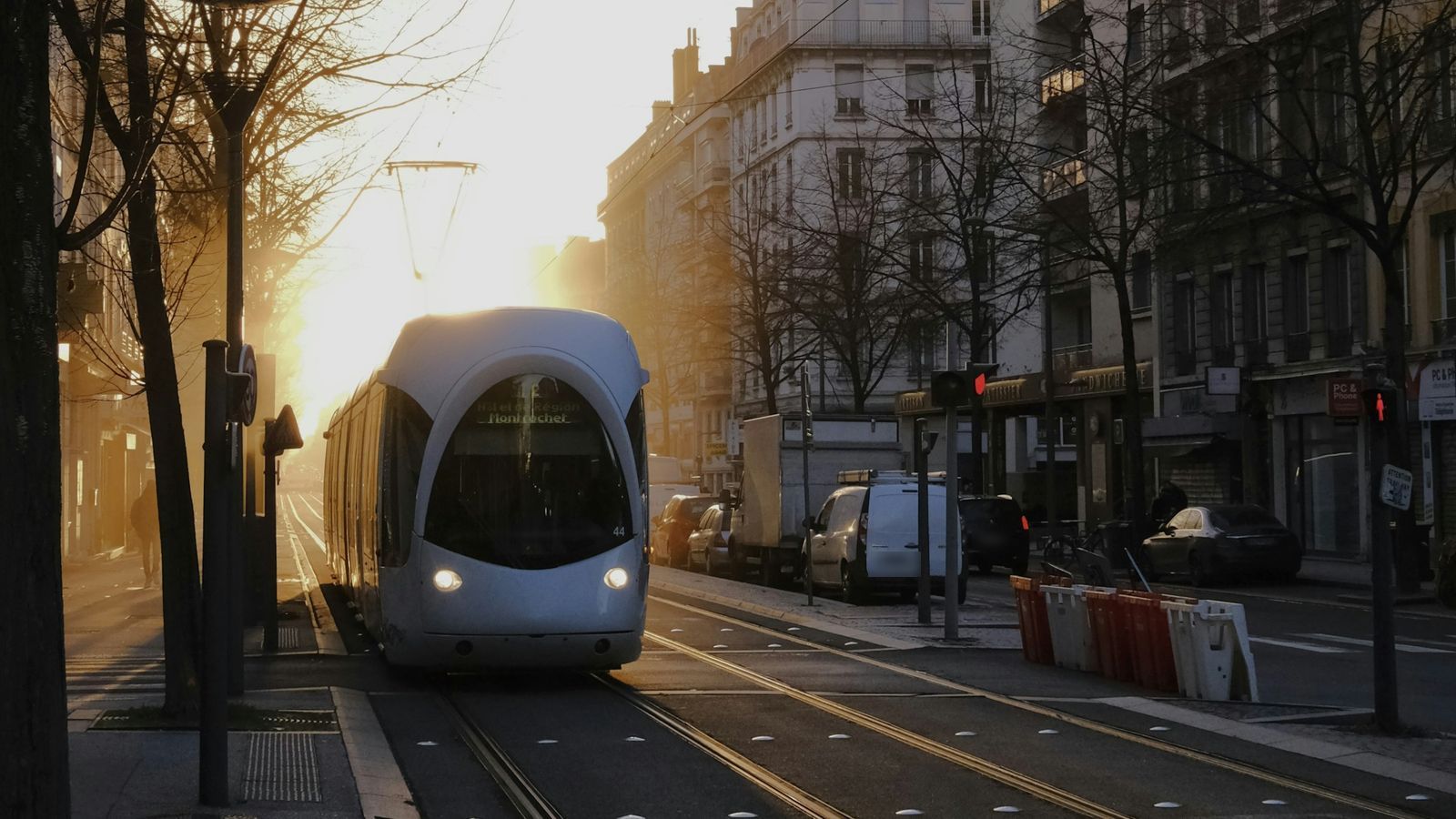 Un tramway lyonnais remonte une avenue bordée d’immeubles, à contre-jour, sous un soleil bas.